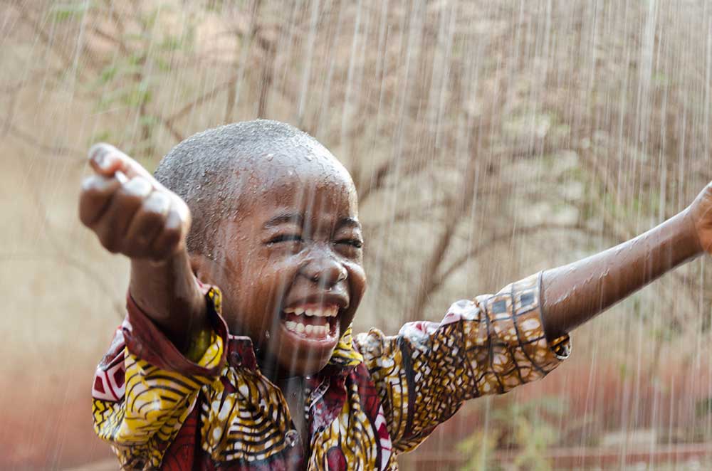 Маленький мальчик стоит на открытом воздухе под дождем
