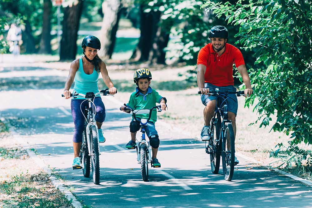 Familia - una dama, un hombre y un niño - andando en bicicleta en un parque